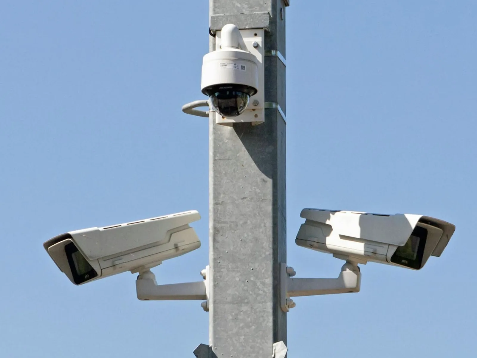 Two bullet cameras and a dome camera on a single concrete pole, covering opposite approaches against a clear sky.